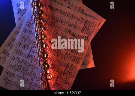 Transverse flute and old sheet music on black table red blue illuminated. Horizontal composition. Top view Stock Photo