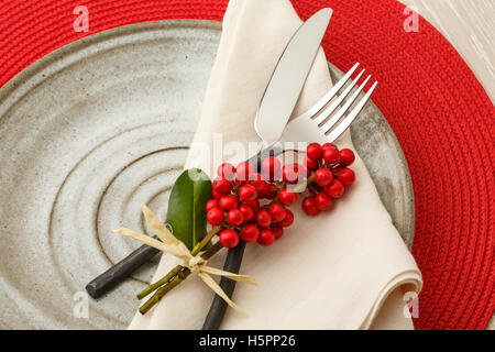 Casual artisanal Christmas table setting place setting with rustic silverware, handmade pottery plate and natural botantical hol Stock Photo