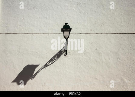 A straight line of a cable on the white wall with a lamp and a the shade of the lamp Stock Photo