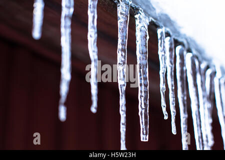 Some ice drops is melting down in the sun at the top of the red roof Stock Photo
