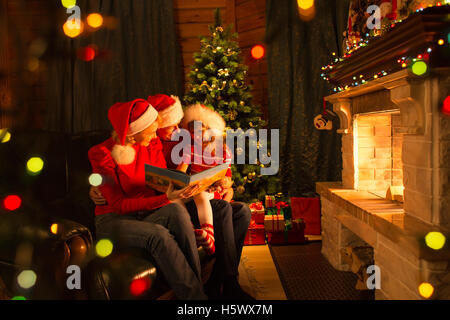 Family read stories sitting on sofa in front of fireplace in Christmas decorated house interior
