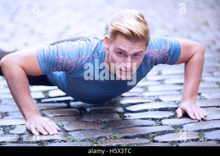 young handsome man doing pushups outdoors on cobblestone Stock Photo