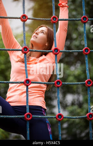 young beautiful sporty woman climbing up a net outdoors Stock Photo