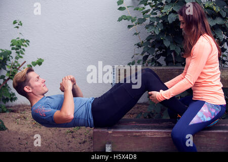 young handsoem man doing sit-ups outdoors with the help of young woman Stock Photo