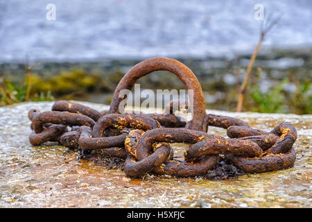 Old rusty metal mooring point with chain attached to concrete block on pier Stock Photo