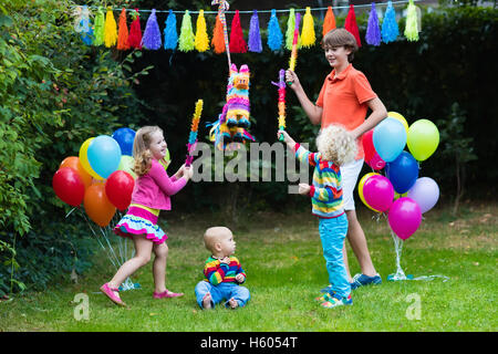 Kids birthday party. Group of children hitting pinata and playing with balloons. Family and friends celebrating birthday outdoor Stock Photo