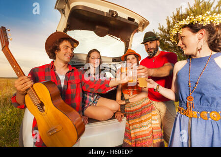 Friends toasting with beer sitting in a car boot Stock Photo