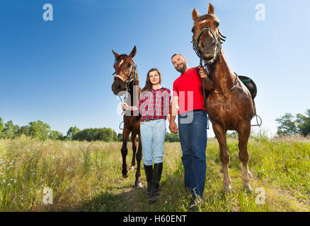 Young couple holding hands and walking with horses Stock Photo