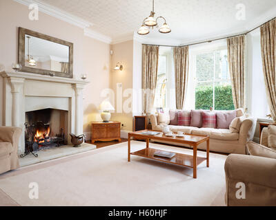A large traditional, homely Victorian livingroom with an impressive fireplace and roaring fire. UK Stock Photo