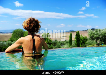 A woman from behind admiring the Tuscan countryside in the pool of the Fonteverde Natural Spa Resort in San Casciano dei Bagni Stock Photo