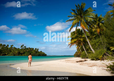 Aitutaki. Cook Island. Polynesia. South Pacific Ocean. A tourist walks along the edge of the palm-fringed beach in One Foot Isla Stock Photo