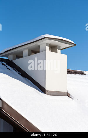 Chimney on roof covered with snow against blue sky Stock Photo