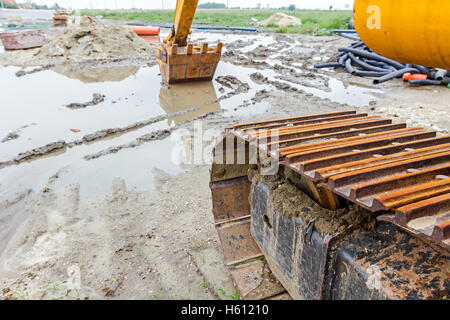 View under the arm of excavator. Reflection on water surface, construction site after rain Stock Photo