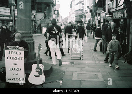 Religious busker with an old guys rule shop sign and street scene at the old cross on Watergate street, in Chester England shot with Kodak BW400 film Stock Photo