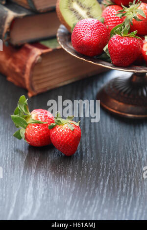 Nice metal bowl full of various fruits on wooden table near old books Stock Photo