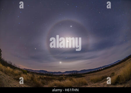 A classic 22° ice crystal halo around the waning crescent Moon, here overexposed, with the Moon between Jupiter and Mars in the Stock Photo