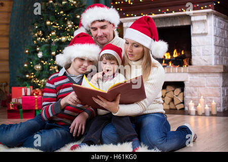 Family read stories sitting on sofa in front of fireplace in Christmas decorated house interior Stock Photo