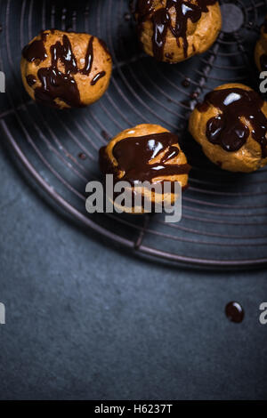 decorating profiteroles with melted hot chocolate on cooling rack Stock Photo