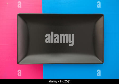 Empty black ceramic dish on over blue and  pink wooden table, rectangle dish Stock Photo