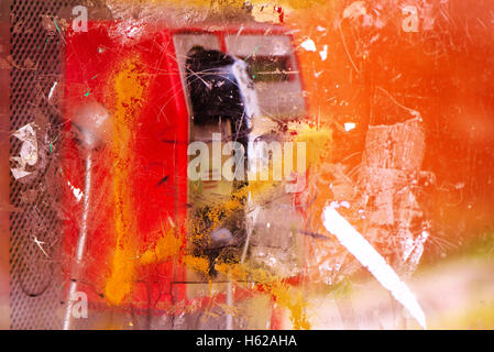 Demolished and vandalized public phone booth on street with graffiti spray marks and stains, selective focus