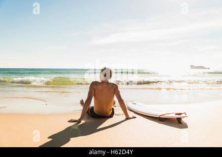 Teenage boy sitting on surfboard at the sea Stock Photo