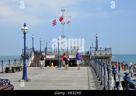 Couple walking with the St Geoge’s Cross, the Merchant Navy Ensign and the Union Jack Flags flying on Swanage pier uk. Stock Photo