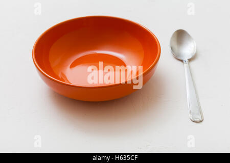 orange bowl and spoon on white plastering plate Stock Photo