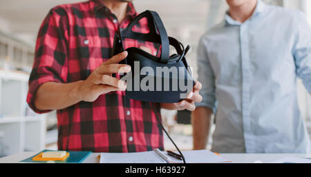 Cropped shot of two young men testing virtual reality headset in office. Business men working at desk holding VR glasses. Stock Photo