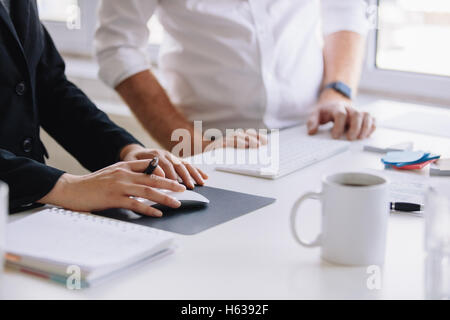 Close up shot of businesswoman using computer mouse with male colleague standing by work desk. Two business associates working t Stock Photo