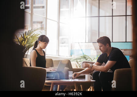 Shot of two businesspeople meeting in lobby area of modern office. Woman working on laptop with man explaining the project plan. Stock Photo
