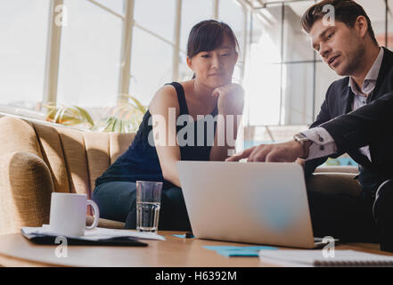 Shot of young woman sitting with businessman pointing at laptop screen. Business partners working together on laptop in office. Stock Photo