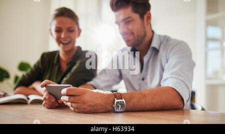 Shot of young man sitting with his girlfriend at table holding smart phone. Young couple at home using mobile phone. Focus on ma Stock Photo