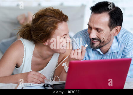 Woman giving earphones to man while lying on bed Stock Photo