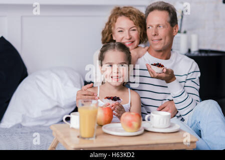 Cheerful little girl holding berry cupcakes with her grandparents Stock Photo