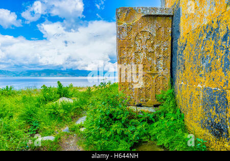 The khachkar (cross-stone) with numerous carved crosses at the Church's wall, with the Sevan Lake on the background, Hayravank,  Stock Photo