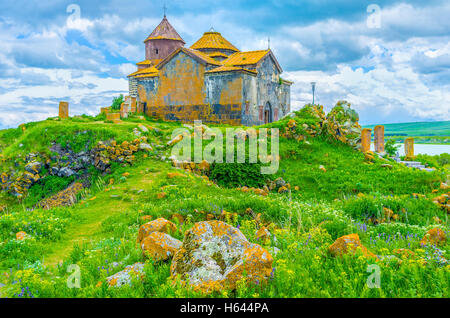 The juicy green hill with bright orange boulders, covered with lichen and moss, topped with the Church of Hayravank Monastery Stock Photo