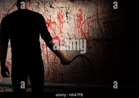 Shadowy figure holding blade near blood stained wall for concept about murder and scary Halloween holiday Stock Photo