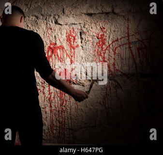 Shadowy figure holding sickle near blood stained wall for concept about murder and scary Halloween holiday Stock Photo