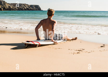 Teenage boy sitting on surfboard at the sea Stock Photo