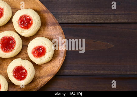 Thumbprint Christmas cookies filled with strawberry jam, photographed overhead on dark wood with natural light (Selective Focus) Stock Photo