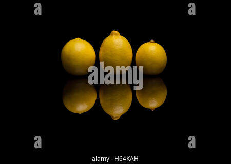 Three whole isolated yellow lemons on black reflective background Stock Photo