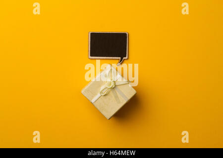 top view of small gift box on yellow background with wooden black chalk board speech bubble for text Stock Photo