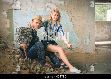 Portrait of a young man and woman in overalls with tools in a newly built house. Concept of construction and home repair. Stock Photo