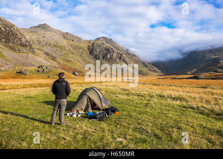 Wild camping in the Upper Esk valley in the Lake District, a young man stands by his tent Stock Photo