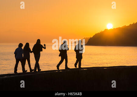 Lyme Regis, Dorset, UK. 25th Oct, 2016. UK Weather. A family walking along The Cobb Harbour wall in Lyme Regis on the Jurassic Coast of Dorset during a misty golden autumn sunset. Picture Credit:  Graham Hunt/Alamy Live News Stock Photo