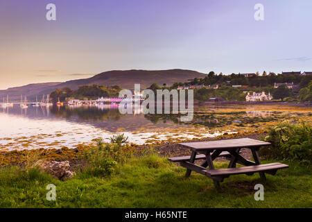 Empty Picnic Table At Portree Bay, Isle of Skye, Scotland During Sunset With View Of Houses And Sail Boats In The Distance Stock Photo