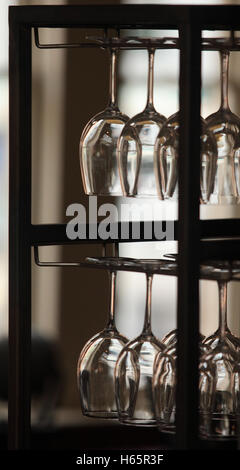 A row of upended wine glasses hanging in a rack, backlit Stock Photo