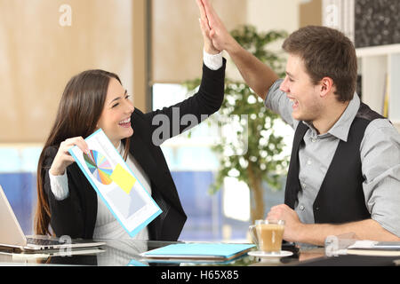 Successful coworker showing a growth graph celebrating good results and giving high five in an office interior Stock Photo