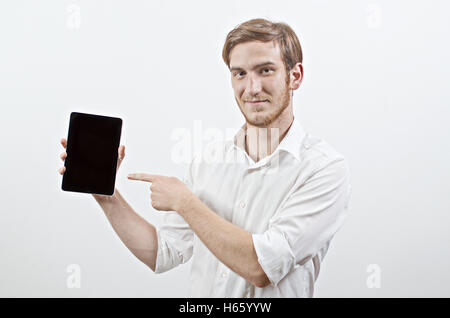Young Adult Man in White Shirt Holds a Tablet and Points to It With His Finger Stock Photo