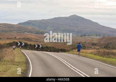 man running along a road on the Isle of Skye in autumn, Scotland, UK Stock Photo
